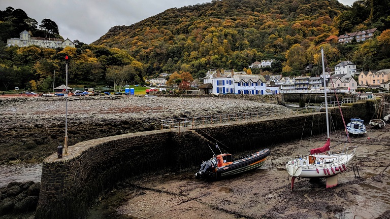 A view of Lynmouth Harbour near Lynton at low tide with boats resting in the dry harbour with the village's shingle beach and fishermen's cottages in the background